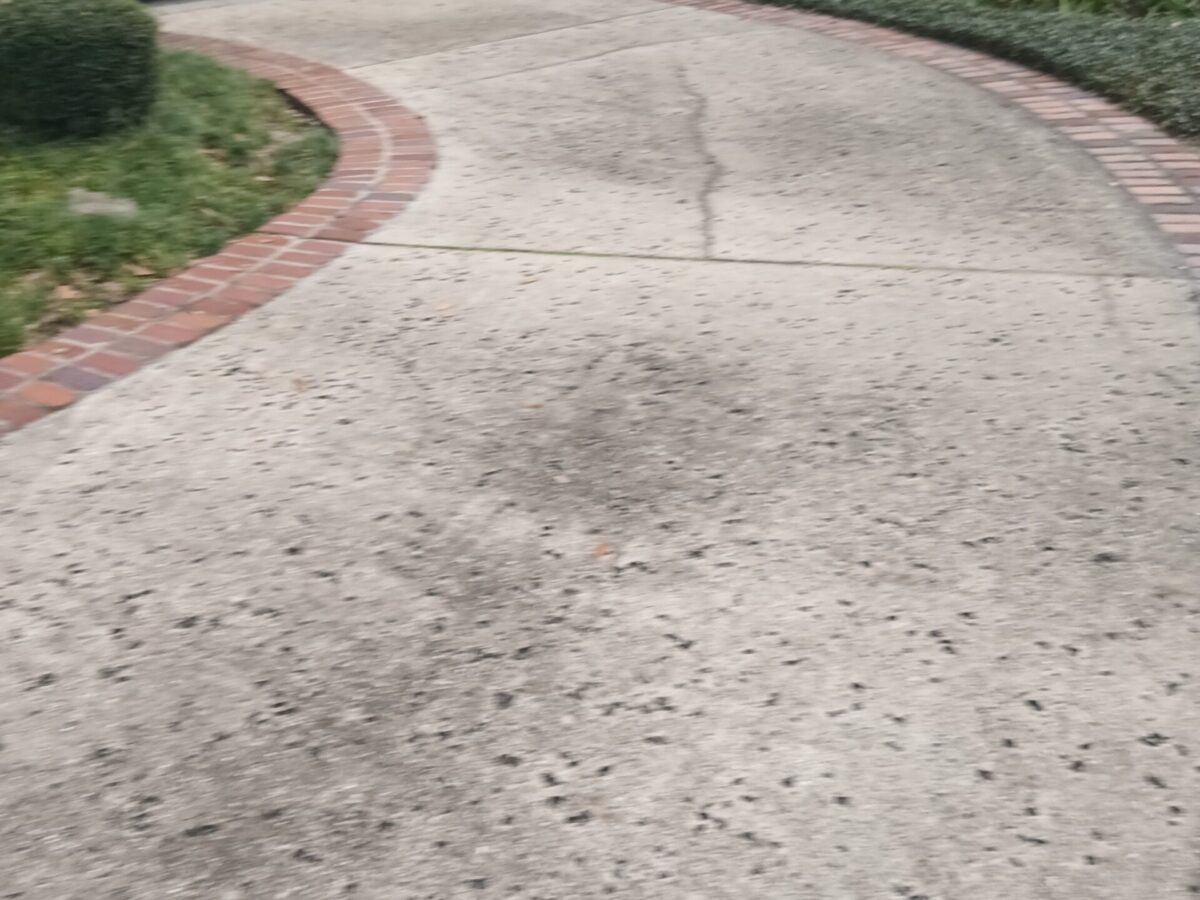 Extended concrete driveway after Pressure Washing in Narcoossee, FL with cleaner pavement near a residential entrance